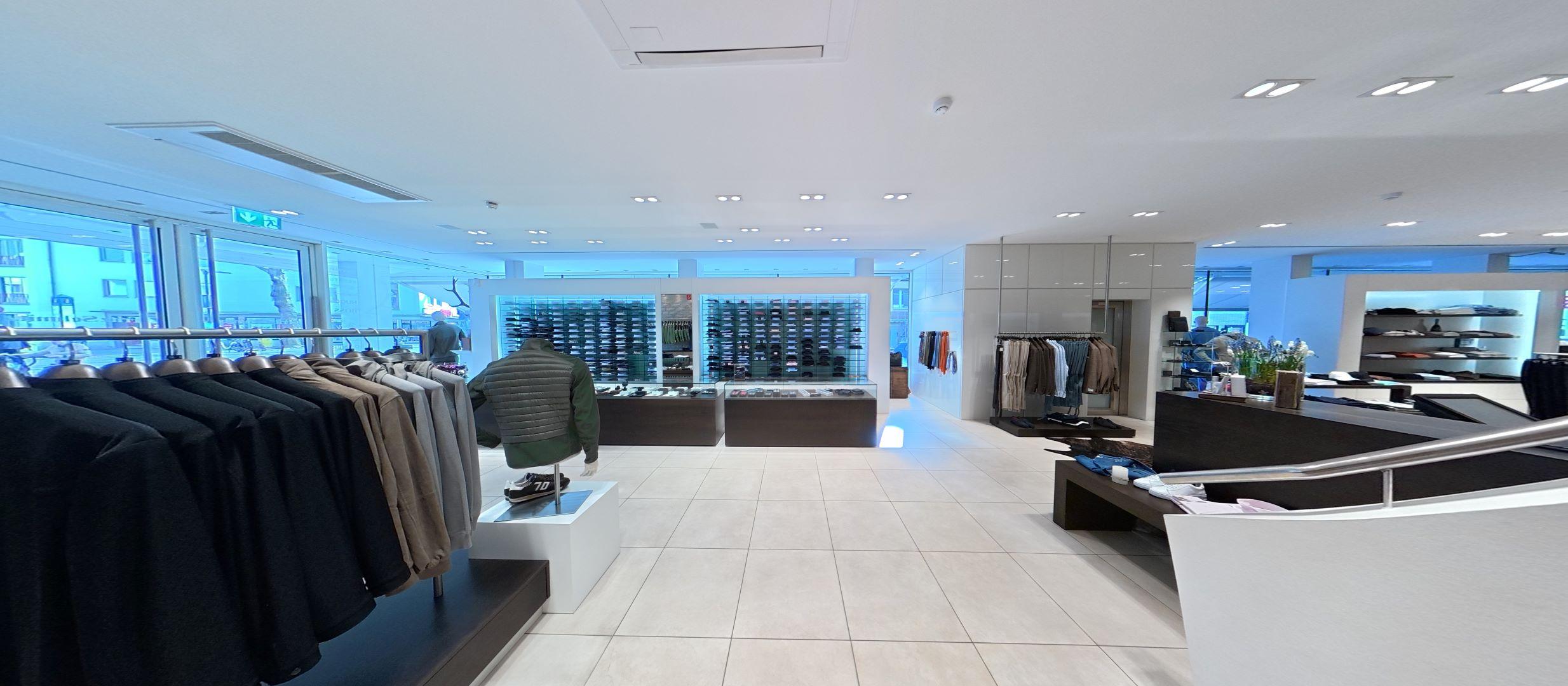 Blick von der Treppe ins Erdgeschoss mit Sicht auf Haupteingang, Jacken, Hemden und weitere Casual-Herrenmode